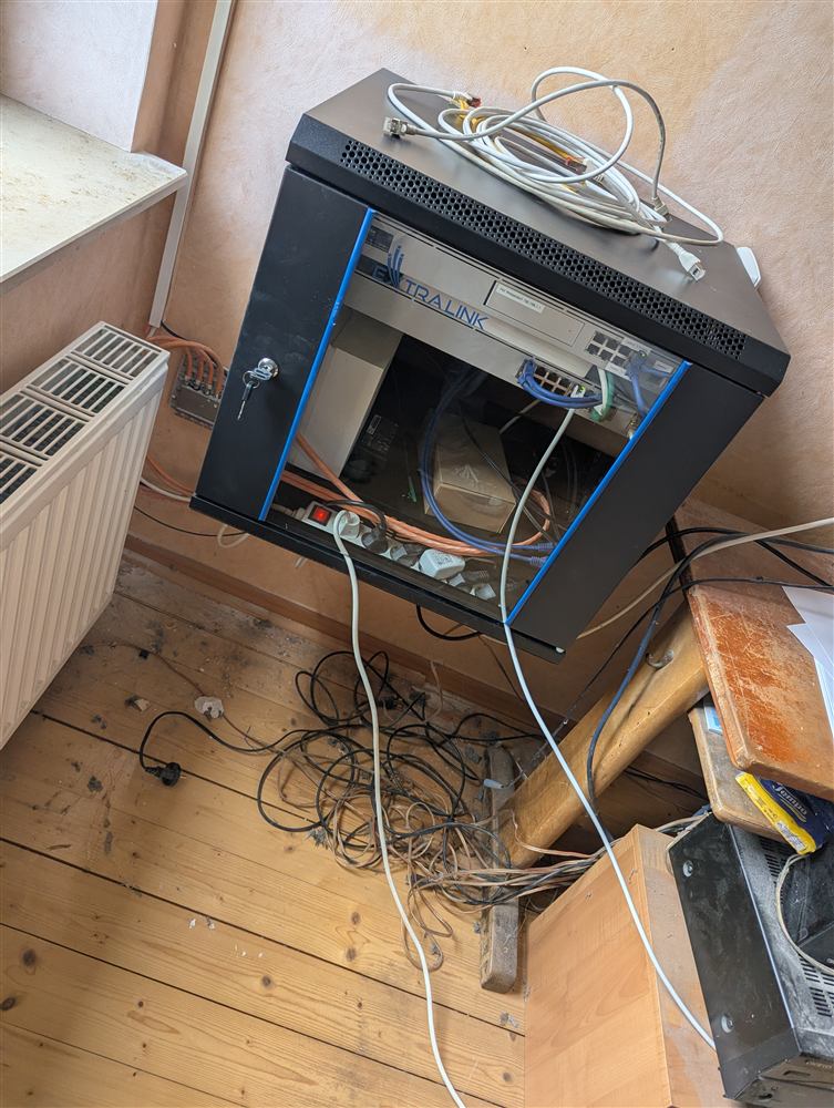 Netzwerkschrank in einem Technikraum mit offen liegenden Kabeln und Zubehör